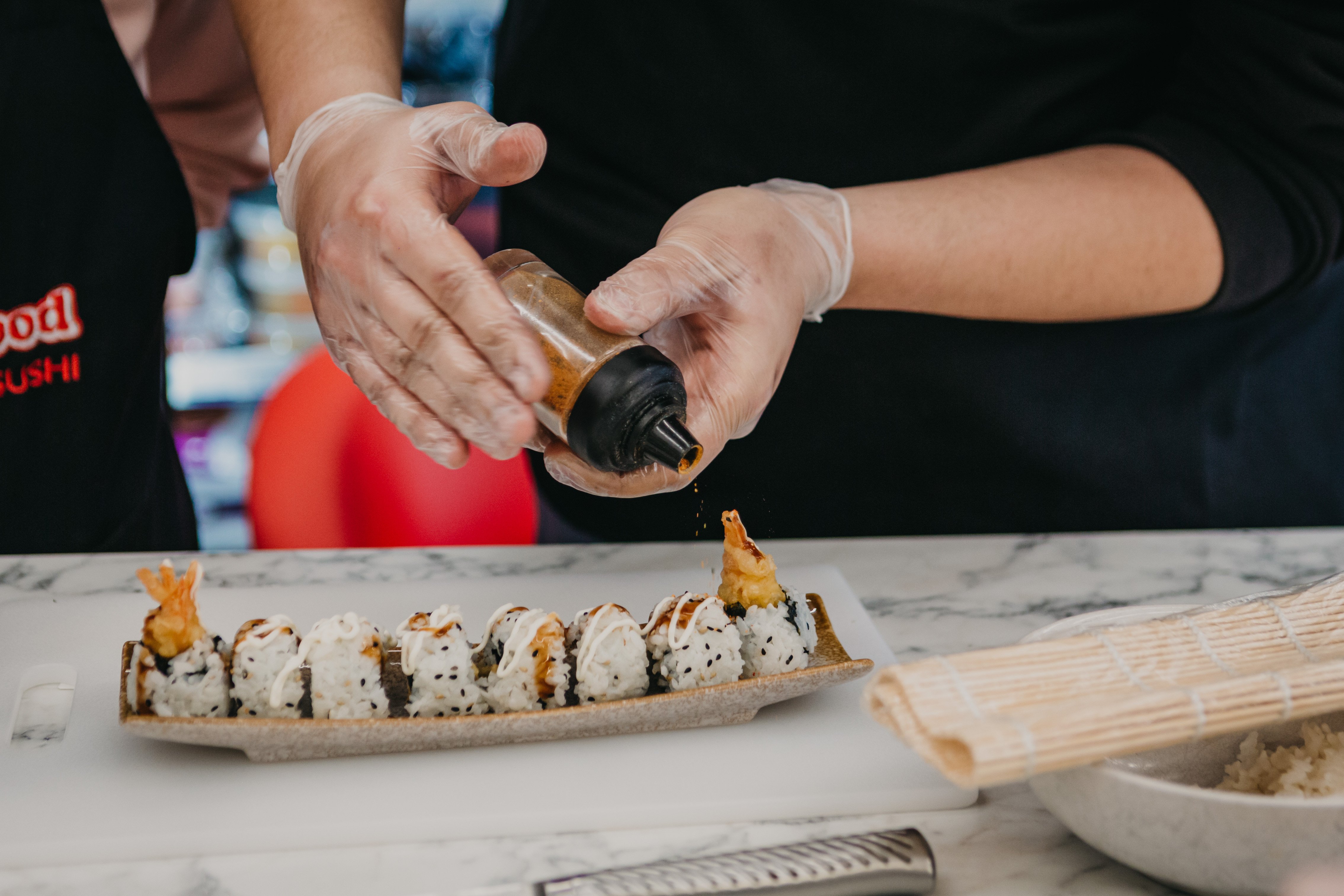 Person applying seasoning to a row of sushi rolls
